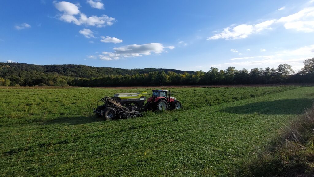 Traktor mit Sämaschine auf grünem Feld, blauer Himmel
