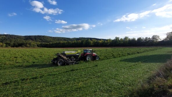 Traktor mit Sämaschine auf grünem Feld, blauer Himmel