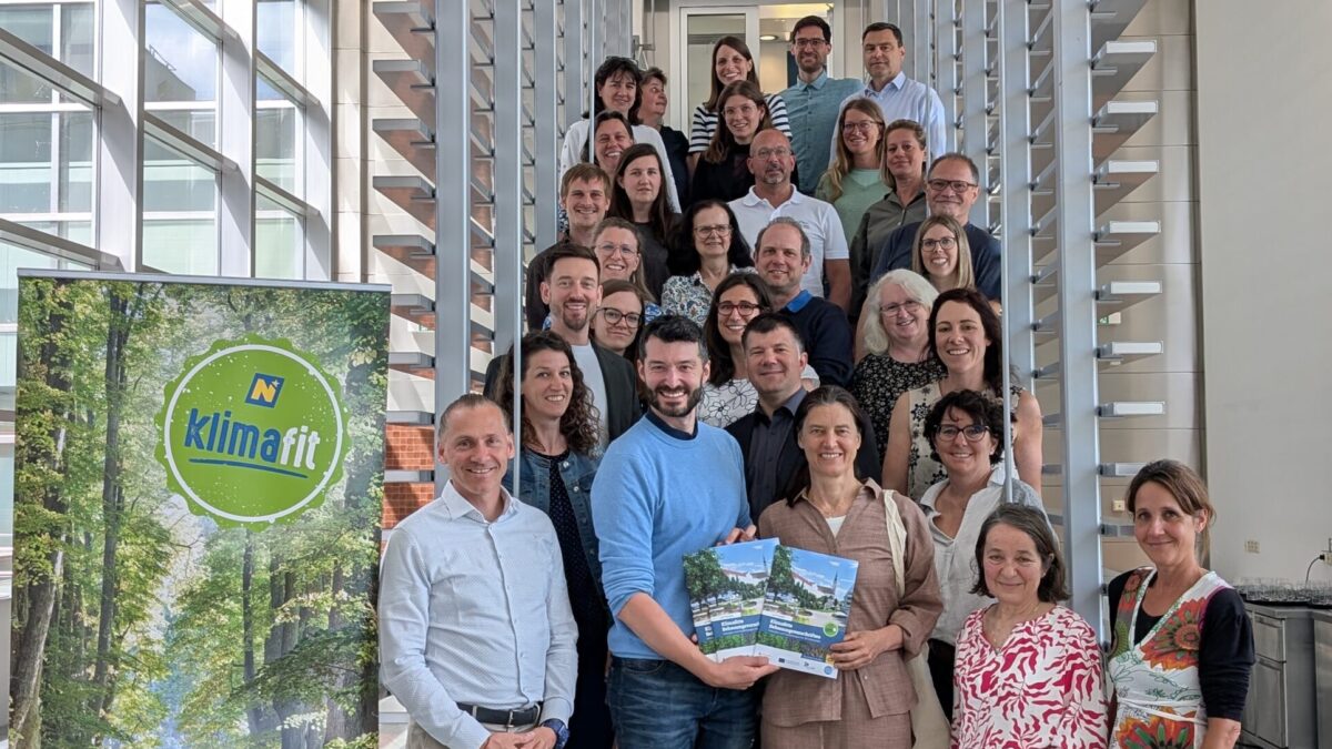 Gruppenfoto mit den NÖ KLAR! Managerinnen und -Managern im Landhaus St. Pölten. Klimafit-Roll Up auf der linken Seite. Die Personen stehen auf einer Treppe.