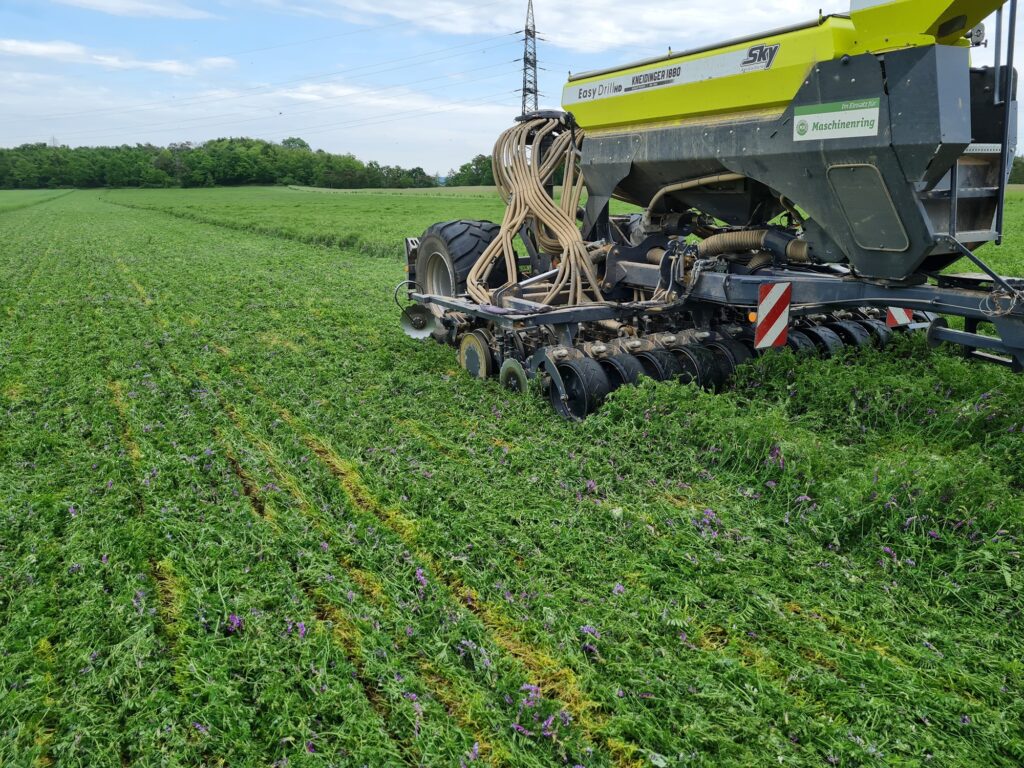 Traktor fährt über grünes Feld, und setzt mit Maschine neue Saat direkt in Begrünung.
