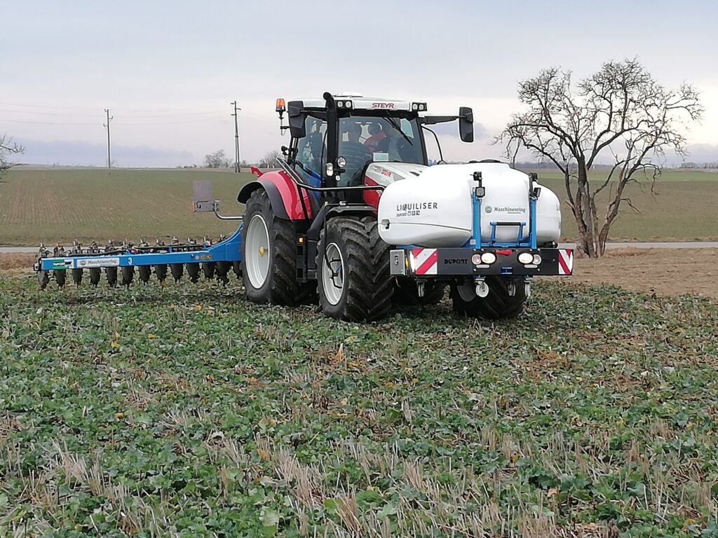 Traktor am Feld, im Hintergrund Stromleitungen