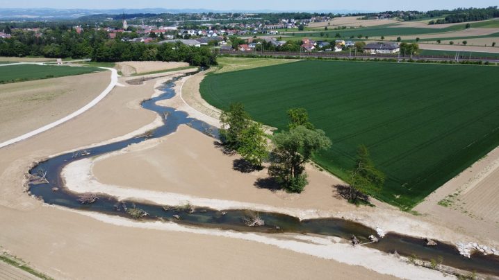 Luftbild, Erlabach schlängelt sich durch die Landschaft, bis jetzt noch nicht bewachsen, daneben ein grünes Feld.
