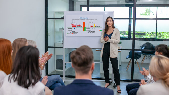 Geschäftsteam mit männlichen und weiblichen Mitarbeitenden im Gespräch bei der Arbeit, die gemeinsam Ideen austauschen und ein Diagramm am Board nutzen. Fröhliche junge Teammitglieder arbeiten zusammen an einer Präsentation am Whiteboard.